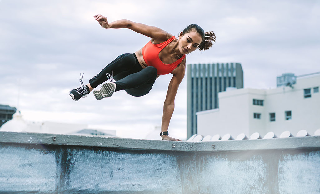 woman-athlete-jumping-over-wall-freerunning-parkour-jumpers-knee