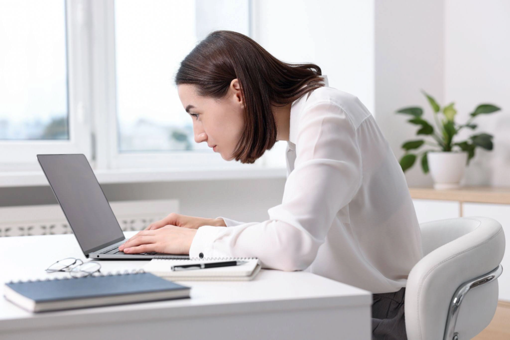 A woman using a laptop, hunched over the screen